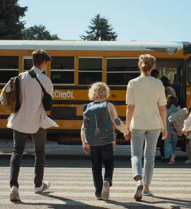 Woman walking hand-in-hand with child to school bus